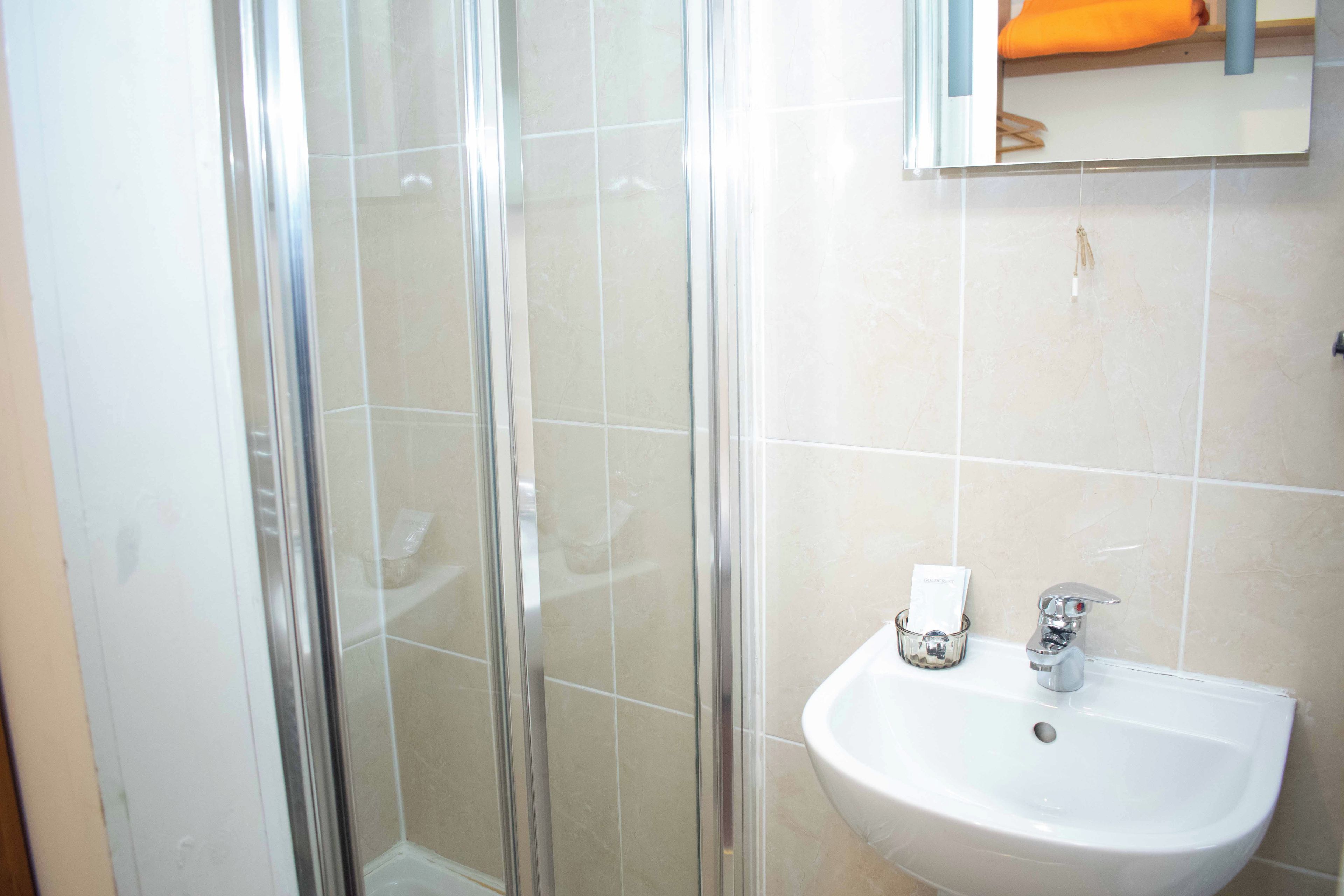A bathroom with a glass shower enclosure, a sink, and a mirror above the sink.