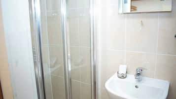 A bathroom with a glass shower enclosure, a sink, and a mirror above the sink.