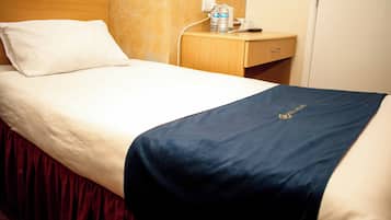 Ett hotellrum med en säng, ett nattduksbord med en vattenflaska, en kopp och en telefon.