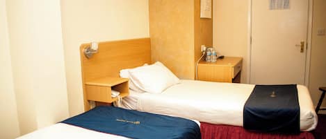 Two single beds with wooden headboards, a bedside table with a phone, a nightstand with a water bottle, and a door with a sign.