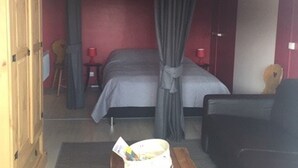 Een kamer met twee bedden, een rode muur, een houten kledingkast en een klein tafeltje met een lamp.