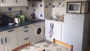 Een kleine keuken met een wasmachine, een magnetron en essentiële apparaten.
