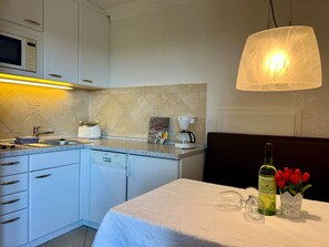 A modern kitchen with white cabinets, a microwave, a coffee maker, and a dining area with a table set for two.
