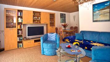 Ein Wohnzimmer mit Fernseher, blauen Möbeln, Holzschränken und einem Chandelier.