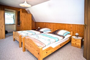 A bedroom with two wooden beds, a nightstand, a lamp, and a window with a view.
