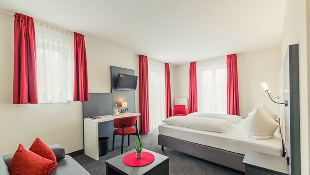 A modern hotel room with a bed, a desk, a chair, and a TV. - Altstadthotel Kneitinger (Abensberg)