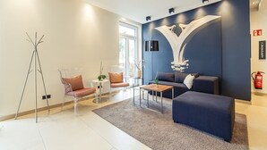A modern living room with a sofa, coffee table, and chairs. There is a large window providing natural light and a decorative wall piece. - Altstadthotel Kneitinger (Abensberg)