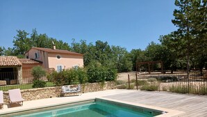 Une piscine avec une terrasse en bois, des chaises longues et un mur en pierre.