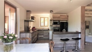 Une cuisine moderne dotée d’un îlot central, d’un coin repas avec une table et des chaises, et d’un bar avec des tabourets.