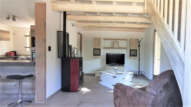 Un salon moderne avec un téléviseur, un canapé et un coin cuisine à l’arrière-plan.