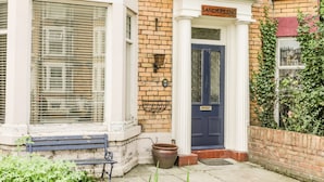 A corner building with a blue door labeled "SANDERLING," a white window with blinds, and a brick wall. - Sanderling (Scarborough)