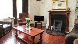 A living room with a fireplace, a television, a coffee table with a vase, and leather furniture. - Sanderling (Scarborough)