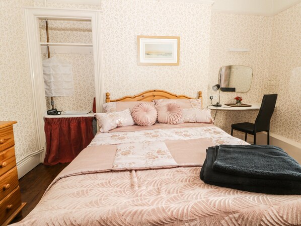 A bedroom with a bed, a wooden dresser, a chair, a desk, and a mirror.