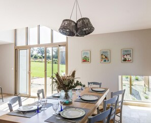 A dining area with a table set for four, large windows, and a view of a garden. - Charming House with Trampoline, Garden, Near Hiking Trails, Sleeps Up to 10 (Gouvets)