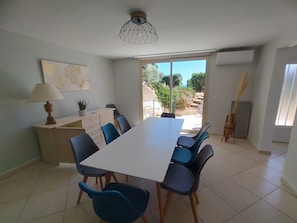 A dining area with a white table and blue chairs, a lamp, a potted plant, and a view of the outdoors. - Stunning new apartment with air conditioning and community pools (Porto-Vecchio)