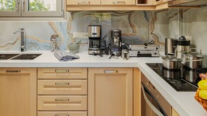 A modern kitchen with light wood cabinets, a marble backsplash, and stainless steel appliances. - Cypress Village - Lux villa 5' from beach (Δαράτσος)
