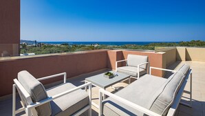 A balcony with white furniture, a small table, and a view of the sea and distant buildings. - Cypress Village - Lux villa 5' from beach (Δαράτσος)