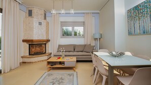 A modern living room with a fireplace, sofa, dining table, and chairs. - Cypress Village - Lux villa 5' from beach (Δαράτσος)