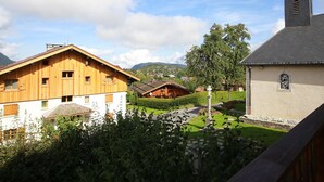 Un chalet de madera con fachada blanca, una iglesia con campanario y un exuberante jardín verde.