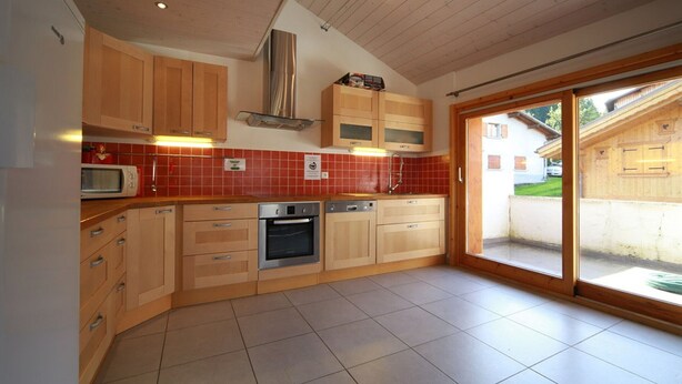 Una cocina moderna con armarios de madera, una campana extractora de acero inoxidable y un salpicadero de azulejos rojos.