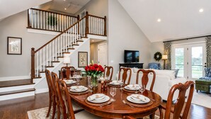 A dining area with a wooden table set for six, a staircase, a living room with a sofa, and a television. - Solon Serenity: A Beautiful, Serene Setting with Mtn Views, Weekly and Monthly Discounts! (Mount Solon)