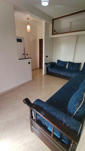 A living room with a sofa set, a wooden coffee table, and a kitchen area in the background.