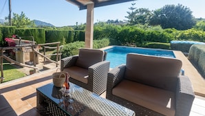 Uma área de estar coberta ao ar livre com dois sofás de vime e uma mesa de vidro, com vista para uma piscina.