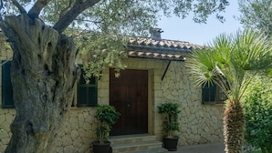 Uma casa de pedra com uma grande  árvore em frente, uma porta de madeira e dois vasos de plantas nos degraus.