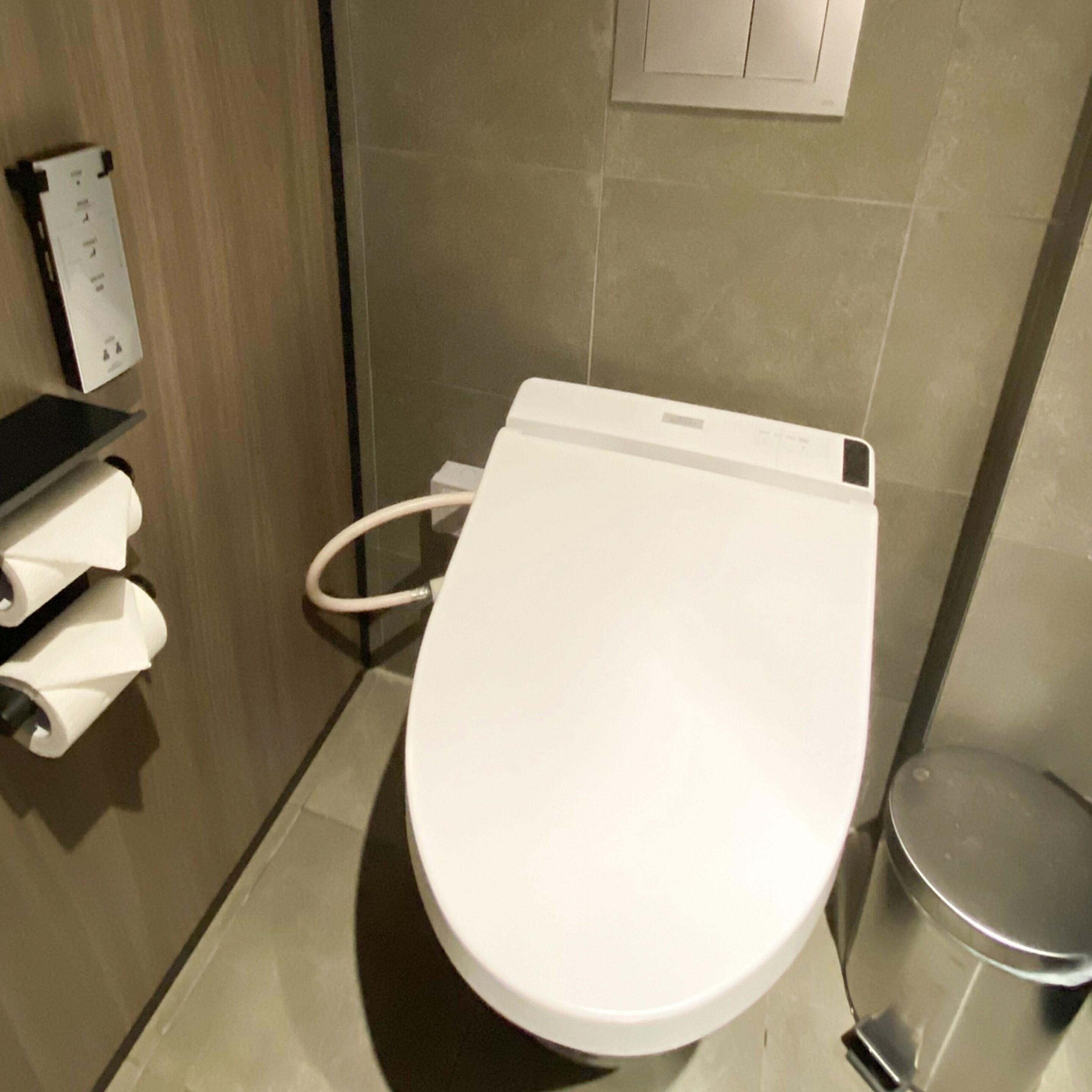 Un baño moderno con inodoro blanco, secamanos y cubo de basura.
