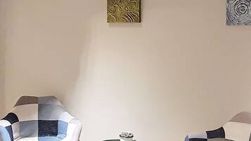 A room with two chairs and a small table, with four artworks on the wall.