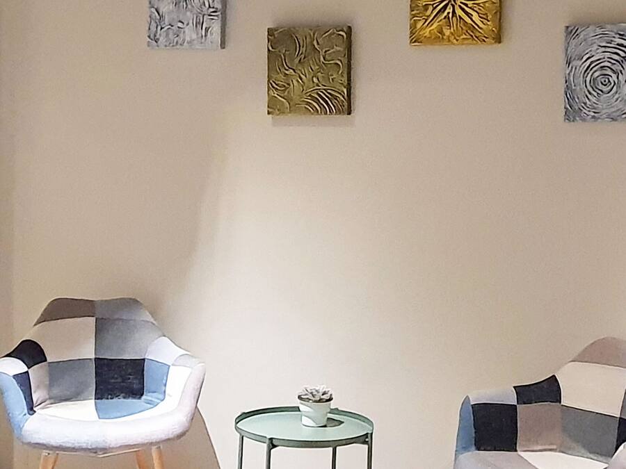 A room with two chairs and a small table, with four artworks on the wall.