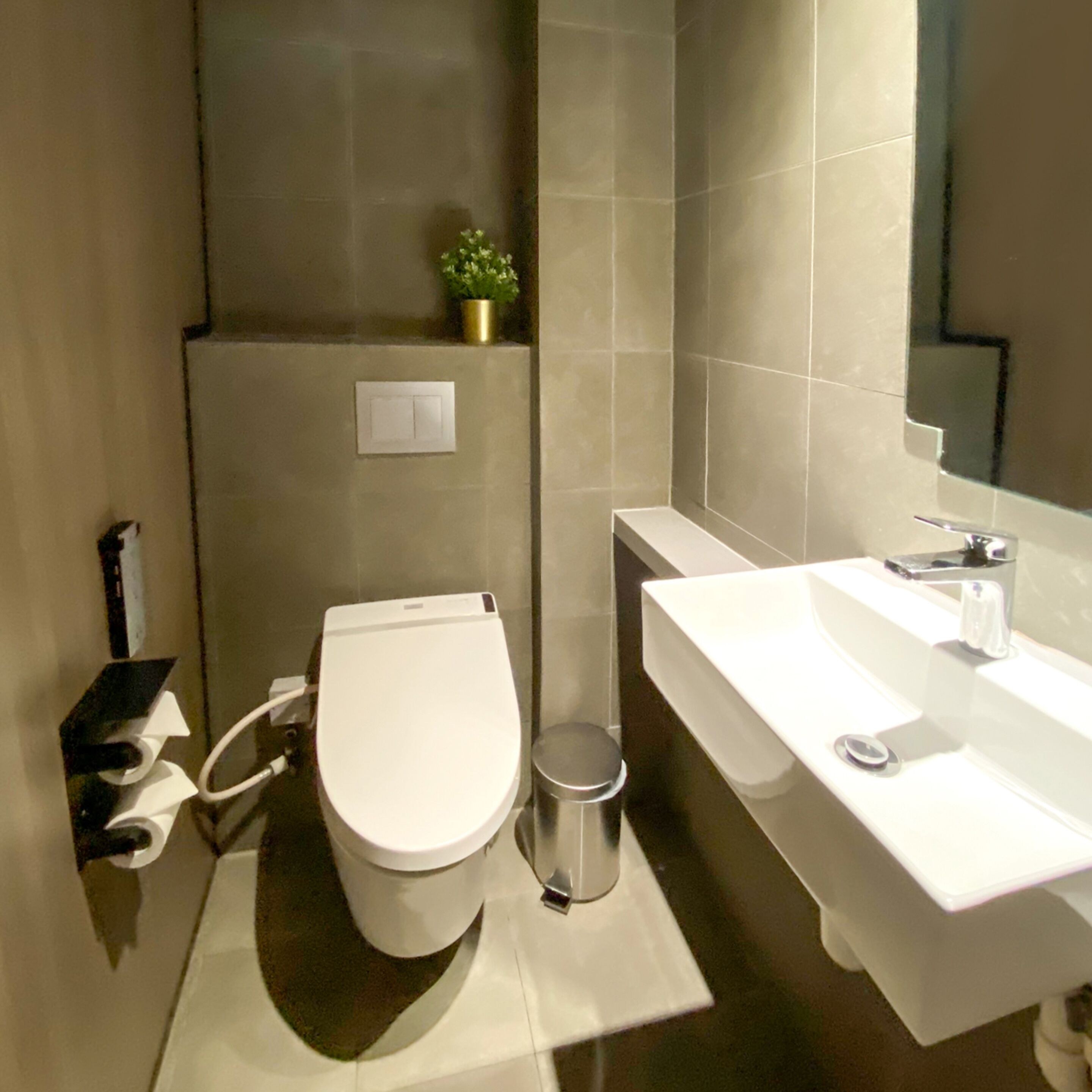 A modern bathroom with a toilet, sink, and a small trash bin.