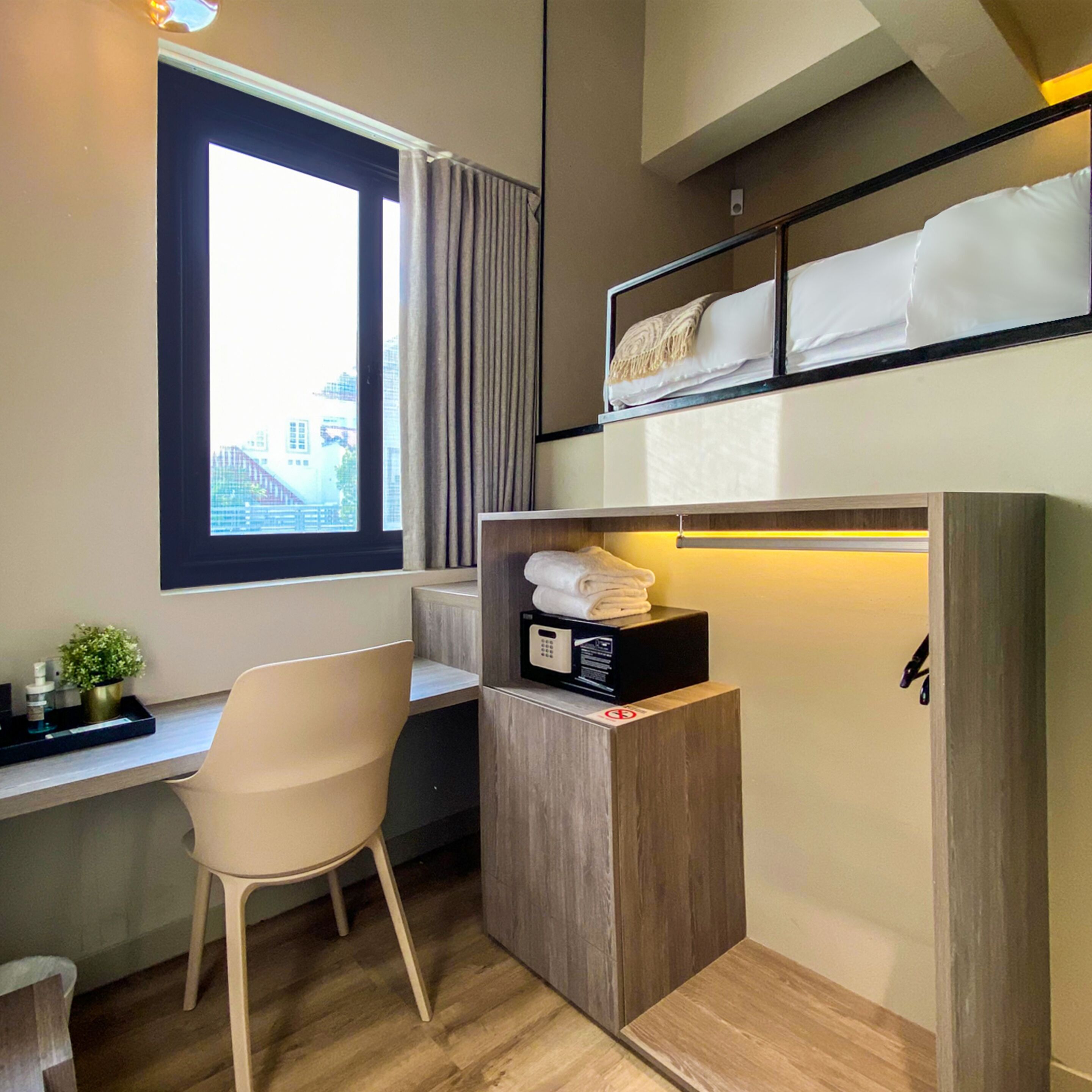 Habitación de hotel pequeña con cama, escritorio, silla y estante con microondas y toallas.