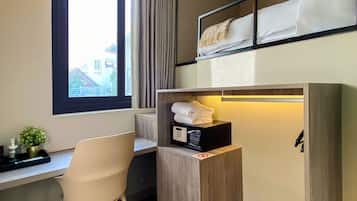 Habitación de hotel pequeña con cama, escritorio, silla y estante con microondas y toallas.