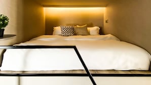 A compact, modern bedroom with a bed centered under a recessed ceiling light, flanked by a small potted plant and a bedside table. - ST Signature Jalan Besar, SHORT OVERNIGHT, 13 hours: 6PM-7AM (Singapore)