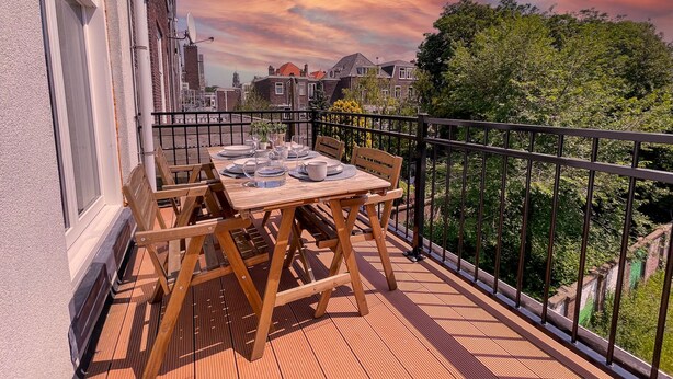 A wooden deck with a table set for dining, surrounded by a black metal railing. - Beautiful luxury apartment (Den Haag)
