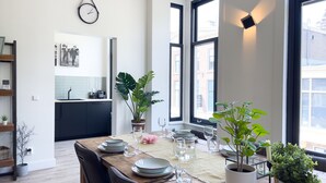 A dining area with a wooden table set for four, surrounded by potted plants and a large window with a view of buildings. - Beautiful luxury apartment (Den Haag)