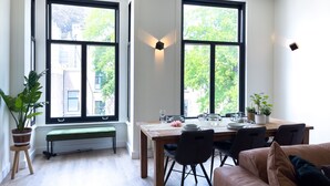 A dining area with a wooden table set for four, surrounded by black chairs, large windows with black frames, and a bench under the windows. - Beautiful luxury apartment (Den Haag)