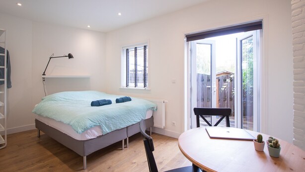 Ein Schlafzimmer mit Bett, Schreibtisch und Stuhl. Ein Fenster mit Jalousien bietet einen Blick ins Freie.