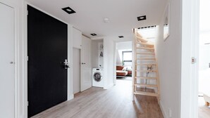Ein Flur mit einer schwarzen Tür, einer Waschmaschine und einer Holztreppe.