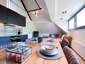 Une cuisine moderne avec un coin repas, comprenant une table en bois dressée avec des assiettes et des verres, un four encastré et une grande fenêtre laissant entrer la lumière naturelle.