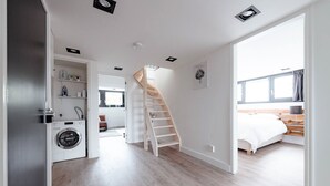 Eine moderne Wohnung mit Waschbereich, einer Holztreppe und einem Schlafzimmer mit großem Fenster.