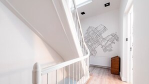 Eine Treppe mit weißen Geländern führt zu einem Raum mit einer weißen Wand und einem großen schwarz-weiß Wandbild einer Karte.
