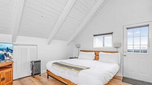 A bedroom with a wooden bed, white walls, a radiator, a TV, and a window with a view. - Ocean Shores cozy chalet located within steps from the beach (Ocean Shores)