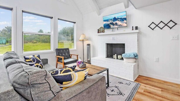A spacious living room with a fireplace, large windows, and a television. - Ocean Shores cozy chalet located within steps from the beach (Ocean Shores)