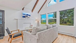 A modern living room with a fireplace, a sofa, a coffee table, and a view of the outdoors through large windows.