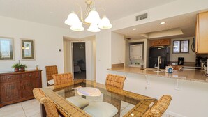 Una cocina moderna con una isla central, electrodomésticos integrados y un comedor con sillas de mimbre y una mesa de vidrio.