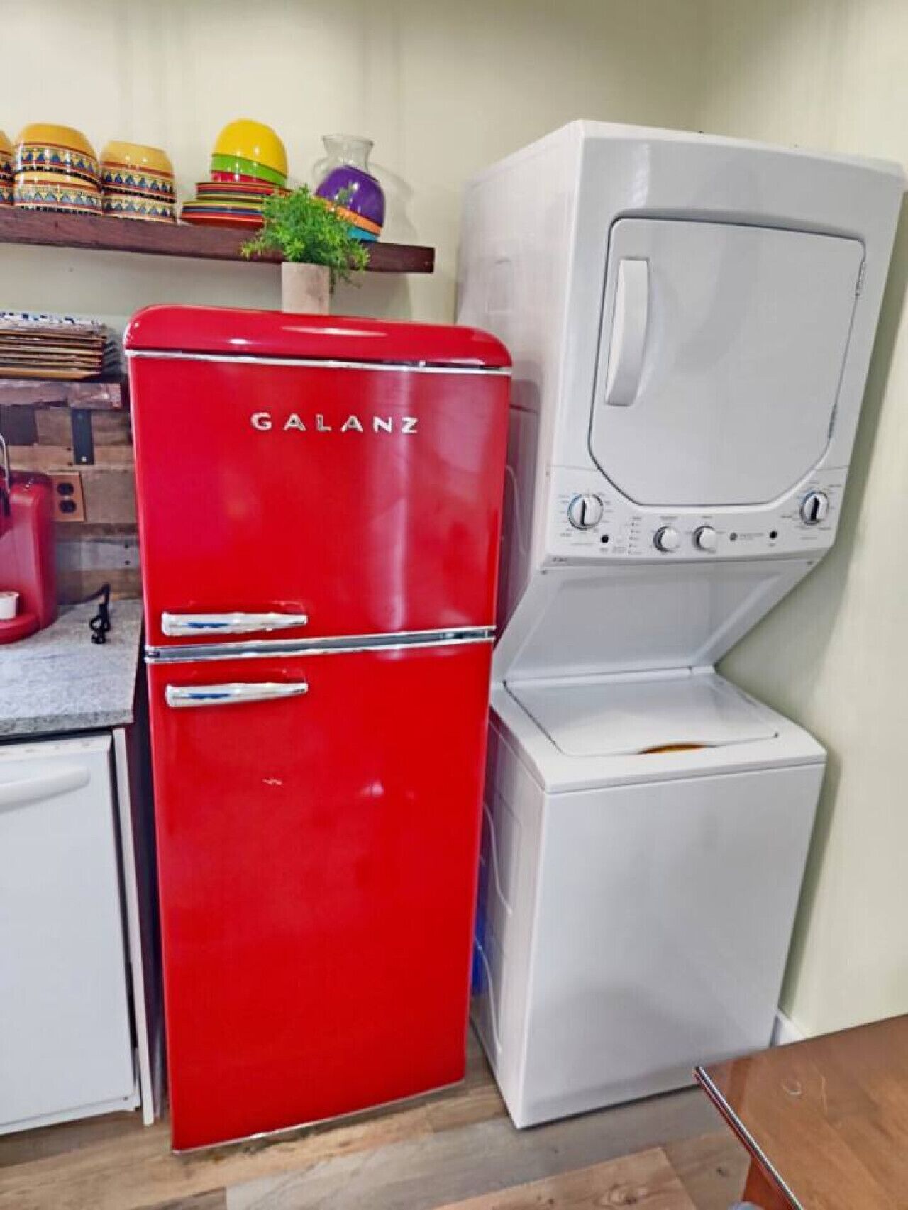 Une cuisine compacte avec un réfrigérateur Galanz rouge, un lave-linge blanc et une étagère contenant des récipients de différentes couleurs.
