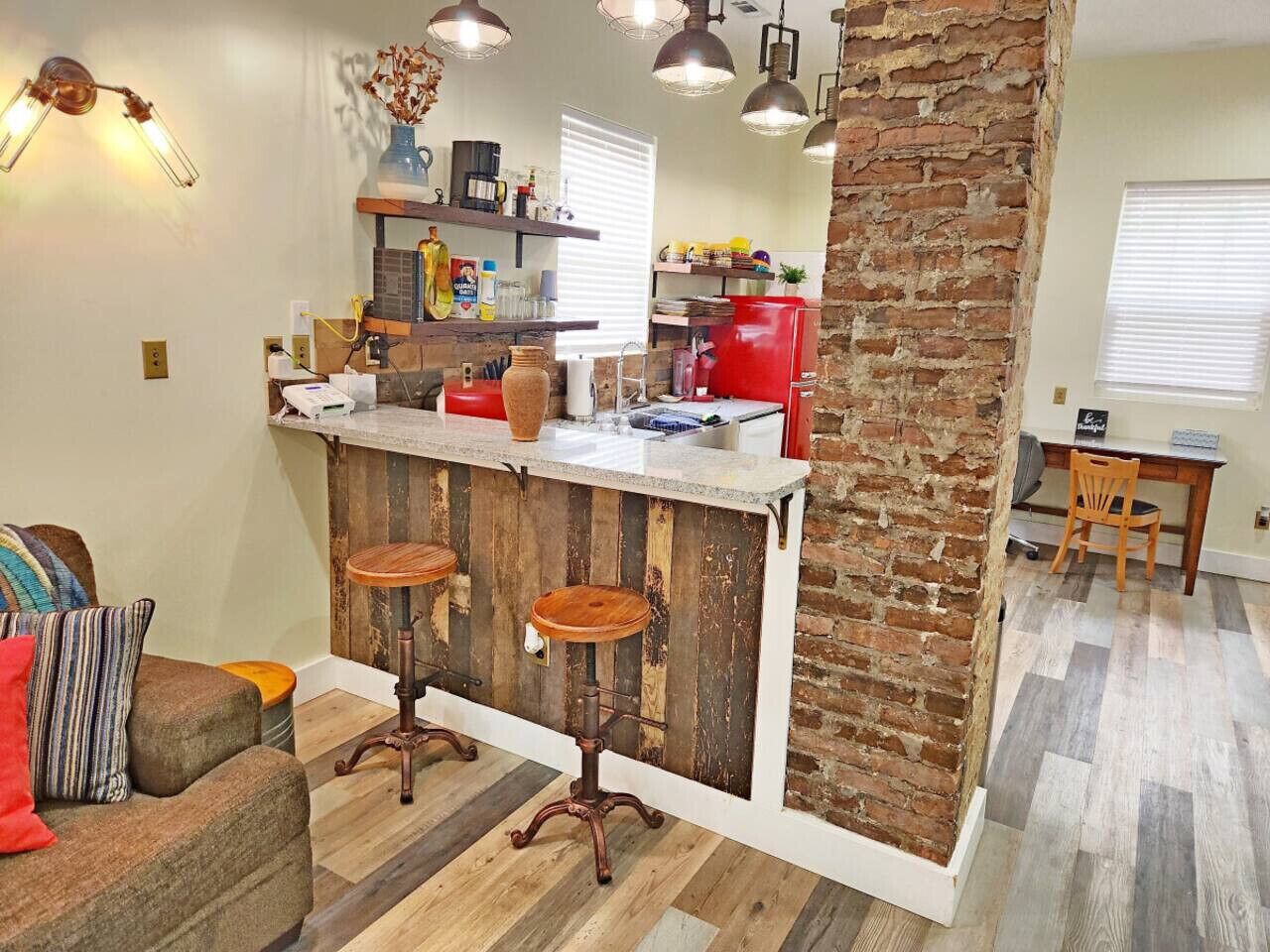 Une cuisine dotée d’un îlot central en bois rustique, de tabourets de bar et d’un mur d’accent en briques.