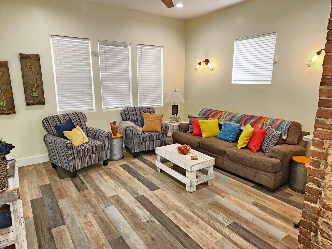 A living room with striped armchairs, a white coffee table, and a brown sofa with colorful cushions.